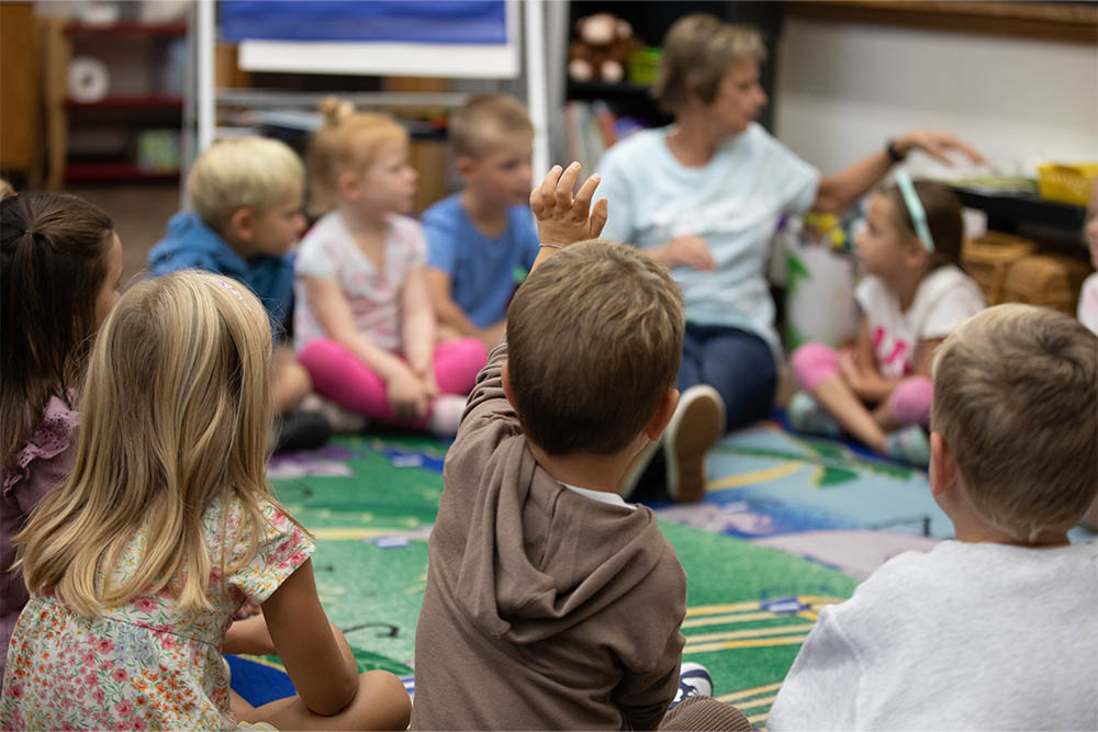 Little boy raising his hand during learning time at HCS, a Christian Preschool in Michigan.