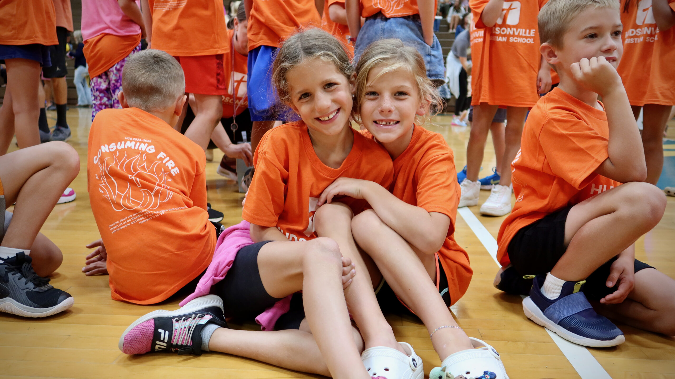 girls hugging in a gym filled with students